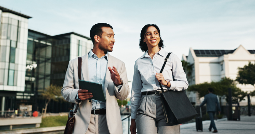 Two professionals walking through a commercial district reviewing a tablet during a commercial real estate advisory discussion