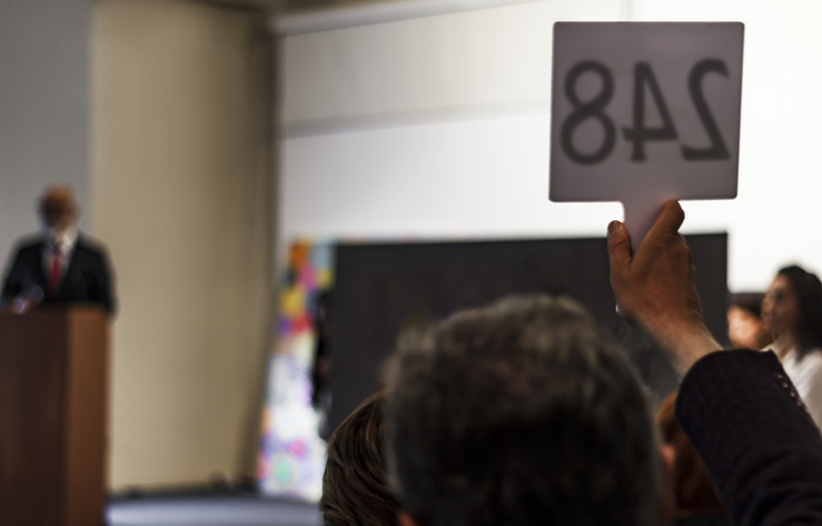 Bidder raises a numbered paddle as an auctioneer leads the room, showing the competitive bidding behind commercial real estate auctions