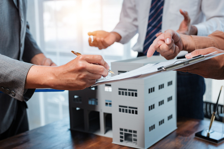Hands signing a purchase agreement beside a building model, with each closed deal adding to commercial real estate transaction volume
